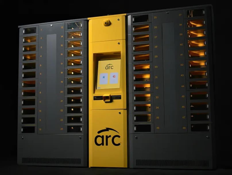 A large, dual-sided ARC smart locker system with a central touch screen and two large panels of numbered compartments on each side. The machine has a distinctive yellow color in the center and the brand logo "arc" at the bottom.