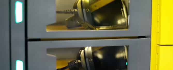 A close-up of three stacked compartments, each containing a smartphone being charged with visible charging cables. The transparent fronts allow the phones inside to be seen. This setup is part of an intelligent locker charging station with a modern design, perfect for effective device management.