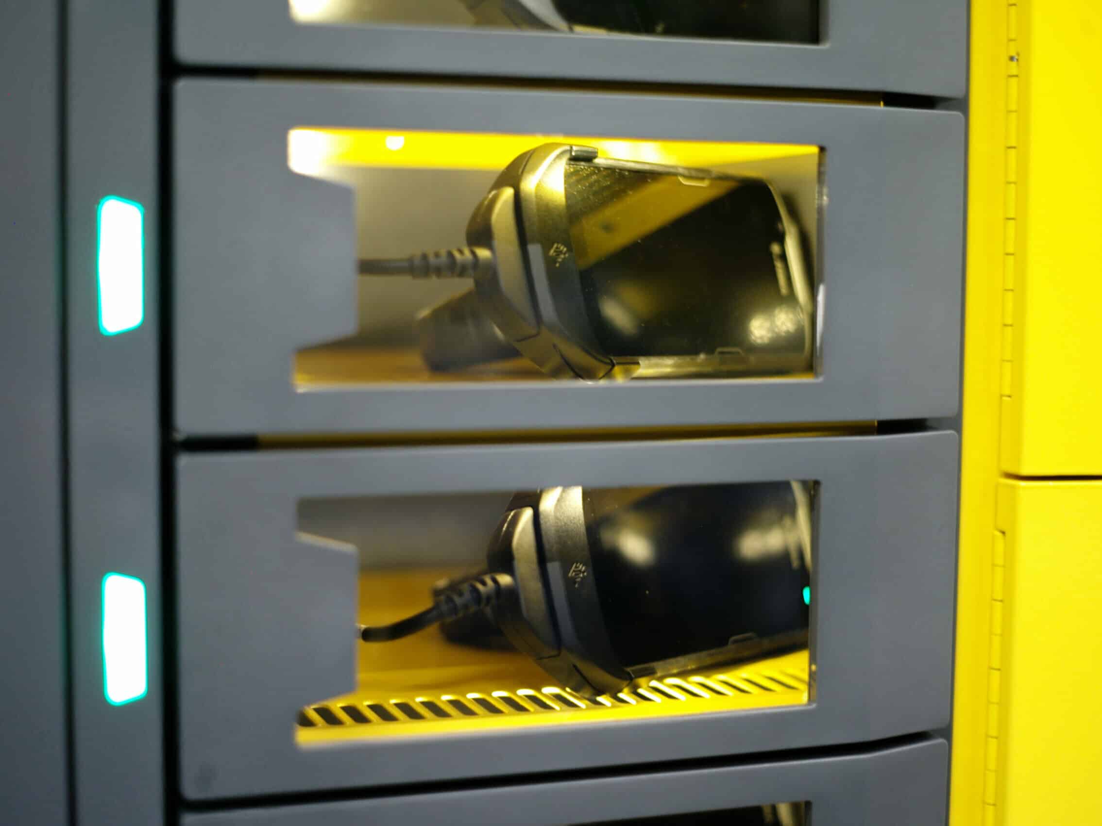 A close-up of three stacked compartments, each containing a smartphone being charged with visible charging cables. The transparent fronts allow the phones inside to be seen. This setup is part of an intelligent locker charging station with a modern design, perfect for effective device management.