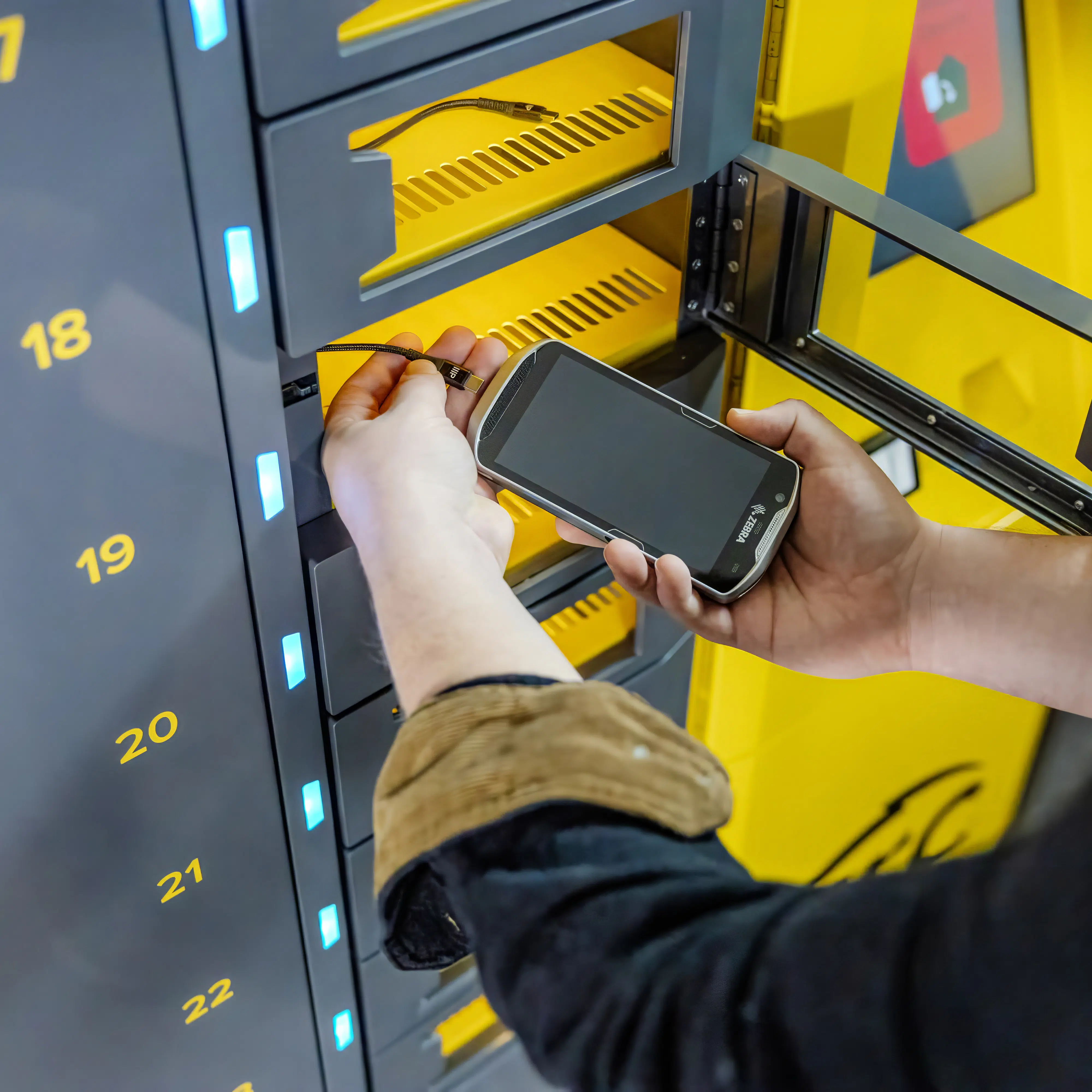ARC-Device Employee placing a Zebra handheld device into a numbered charging locker at an ARC smart kiosk.