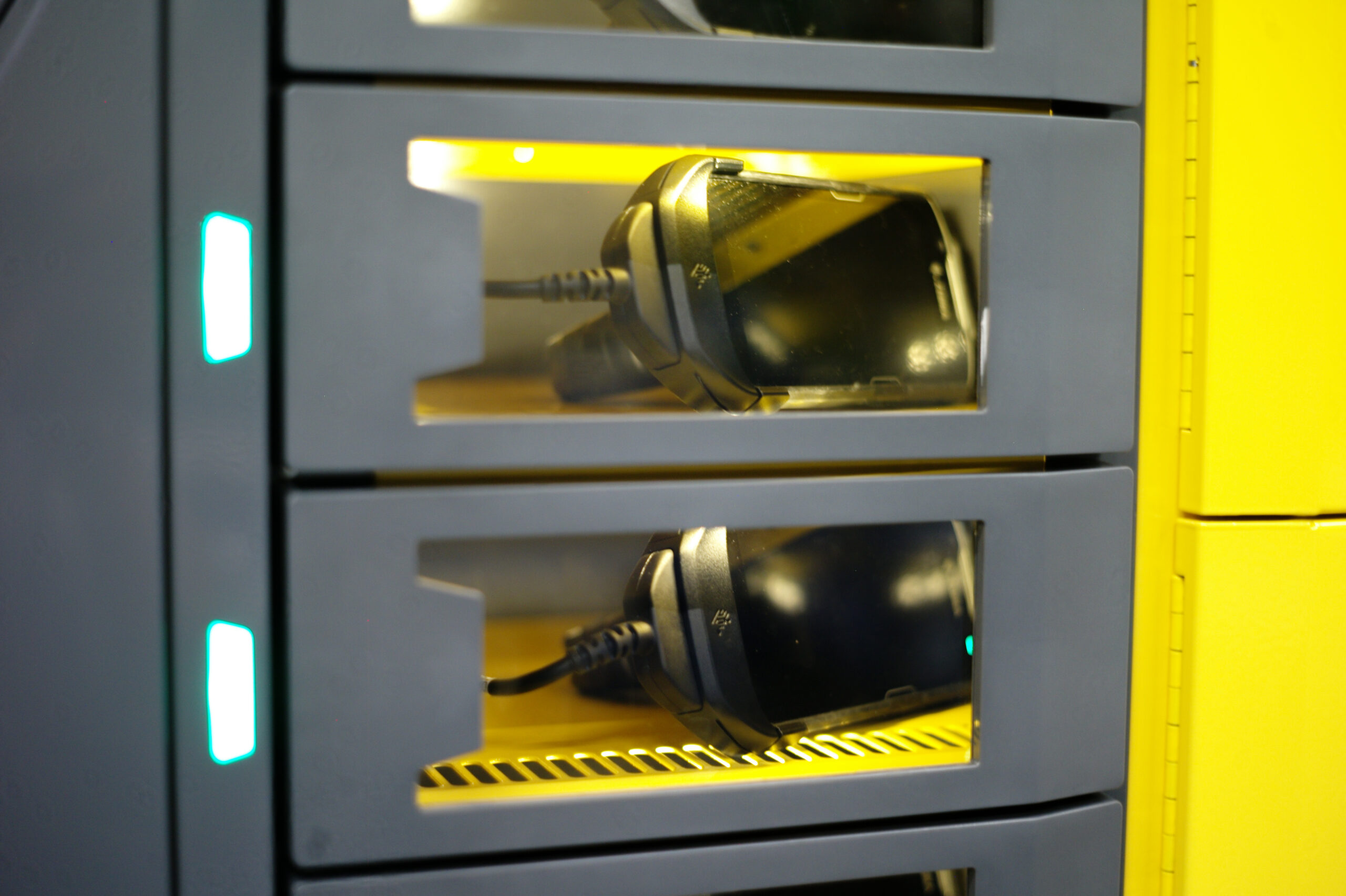 A close-up of three stacked compartments, each containing a smartphone being charged with visible charging cables. The transparent fronts allow the phones inside to be seen. This setup is part of an intelligent locker charging station with a modern design, perfect for effective device management.